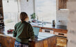 © olezzo - Woman in sweater standing in rustic wooden kitchen using laptop at home