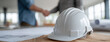 © sam richter - White safety helmet rests on architectural blueprints at construction site.
