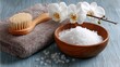 © Taisiia - A wooden bowl filled with sea salt for spa treatments, accompanied by a folded towel, a brush, and a delicate orchid branch for a relaxing, luxurious atmosphere