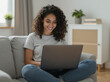 © Đào Tuấn Anh - Smiling Young Woman With Curly Hair Using Laptop Sitting Cross Legged On Sofa At Home