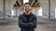 © Vasiliy - Confident young athletic man smiling at the camera with arms crossed. Portrait of a happy male in an urban city setting under a bridge