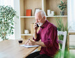 © Lumos sp - Portrait of a senior mature man or businessman working from home office using smart phone and readin ga document at home