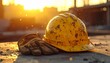 © nupixel - Industrial safety concept. Yellow construction hard hat and leather work gloves resting on a concrete surface at a construction site with warm golden sunset light and dust particles.