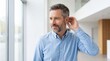 © Janna - Mature man adjusting hearing aid near window in modern interior with copy space