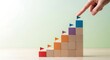 © Shapla - Hand positions a blue block with an attached flag on a rising wooden staircase, illustrating business growth, sequential progress, and the attainment of strategic objectives.