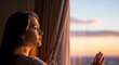 © Angavlan - Young woman opening curtains and looking out window at sunset. Profile of female face in golden hour light. Concept of hope and dreaming
