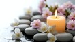 © Yuliia - Zen spa composition with burning candle, smooth stones and delicate pink cherry blossoms on white surface for relaxation and wellness treatments.
