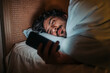 © Akbari - Man lying in bed at night, looking at his smartphone, suggesting themes of sleeplessness, technology use in the bedroom, or potential negative impact.