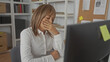 © Krakenimages.com - Woman with hand on cheek resting at desk by computer monitor in office, eyes closed and slumped posture, corkboard and shelves visible; fatigue.
