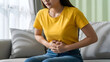 © ANMZAKARIA - Young woman suffering from severe abdominal pain and stomach ache at home | Female having intense period pain or menstrual cramps on sofa | Indigestion, gastritis, or food poisoning health issue