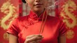 © 69 - Woman in traditional red dress holding incense sticks with smoke against decorative background of dragons and cultural symbols