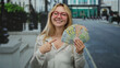© Krakenimages.com - Young woman with glasses smiling and pointing at romanian lei banknotes on a city street, showcasing vibrant currency in an outdoor urban setting with modern architecture.