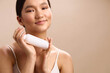 © SHOTPRIME STUDIO - asian woman holds a skincare bottle near her cheek in a clean studio setting, soft lighting and relaxed smile convey skincare confidence, beauty wellness vibe.