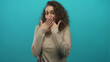 © Krakenimages.com - Young hispanic woman covering her mouth with both hands in turquoise studio mid gesture, curly hair framing face; surprise.