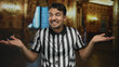 © Krakenimages.com - Young hispanic man wearing referee uniform making uncertain gesture inside museum with ornate decor suggesting confusion or doubt amid elegant setting.