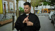 © Krakenimages.com - Man dressed as priest standing on urban street with humorous gesture in background of a cityscape, showcasing religious attire and casual demeanor.