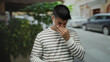 © Krakenimages.com - Young man in striped shirt covering nose while standing in a city street during the day.