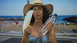 © Krakenimages.com - Woman in bikini and hat cooling with fan holding water bottle at sunny seaside beach.
