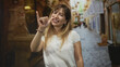 © Krakenimages.com - Woman smiling holds pinky finger up in a narrow cobblestone street with fountain and storefronts in view; playful promise.