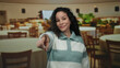 © Krakenimages.com - Woman smiling in a cozy restaurant with ambient lighting and wooden chairs gives a friendly point towards the camera, creating a warm inviting atmosphere indoors.