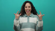 © Krakenimages.com - Young hispanic woman making rock gestures while sticking out tongue against green wall background in a playful manner.