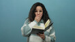 © Krakenimages.com - Hispanic woman with curly hair and glasses is reading a book, showing surprise against an isolated blue background wall.
