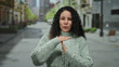 © Krakenimages.com - Woman making timeout gesture on city street wearing green sweater outdoor signaling pause or stop with focused expression in urban environment during daytime.