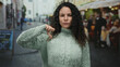© Krakenimages.com - Woman gesturing on outdoor terrace with curly hair wearing sweater expressing emotions on street surrounded by cafes and people in the background during daytime.