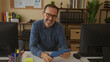 © Krakenimages.com - Senior hispanic man in glasses using tablet in modern office setting with organized desk, surrounded by computer, stationery, and shelves for business productivity and focus.
