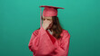 © Krakenimages.com - Woman in pink graduation gown standing over green background looks thoughtful and contemplative, symbolizing a young student's introspection on achieving success.