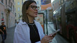 © Krakenimages.com - Young woman texting on smartphone with hands, wearing glasses and a white shirt on a rome street while looking at screen; urban concentration.