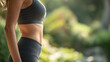 © Ally_art - Profile view of a young Caucasian woman's slim and toned stomach in grey activewear against a blurred outdoor background.