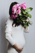© Nataliya - Vertical portrait of a pregnant Caucasian girl in a knitted dress with a bouquet of roses in her hand.
