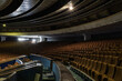 © Aimur - An empty vintage auditorium inside an abandoned city hall building with brown upholstered theatre seats. Decaying municipal assembly hall featuring curved rows and concrete brutalist architecture