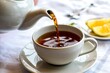 © RIKON - A warm cup of tea being poured from a teapot onto a saucer with lemon slices in the background