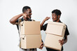© SHOTPRIME STUDIO - Two african men with dark skin holding cardboard boxes and smiling while standing against white background for delivery and moving concept.