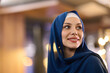 © .shock - Smiling Woman in Blue Hijab Outdoors at Night With Warm City Lights Behind