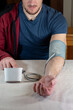 © Pat dream - Man using a digital blood pressure monitor at home. Close up of a person sitting at a table with an automatic arm cuff for health monitoring, hypertension prevention and medical self-diagnostic.