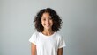 © Vadym - Smiling teen girl with curly dark hair wears white t-shirt. Studio portrait, light grey background. Youthful person looks directly at camera. Copy space available for text.