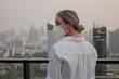 © blackday - Woman wearing protective face mask standing on rooftop with modern city skyline