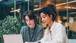 © mila103 - Two women work together at a laptop in a modern office. They share ideas and focus on the screen in the late afternoon light. Plants surround them.