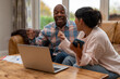 © Iryna - Two people engage in lively discussion at home while seated on a couch with a laptop