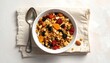 © iso - A close-up, top-down view of a bowl of granola with dried fruit and nuts, next to a spoon on a folded cloth