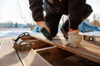 © True Pixel Art - A tradesperson in gloves kneels on timber joists, driving screws into composite decking as a level and staple gun rest nearby on a cold day with snow and bare trees.