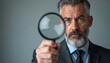 © Pete - Serious man in suit holds magnifying glass close to camera. He intently searches for detail. Mature person with grey hair and beard looks closely for clues.