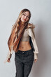 © SHOTPRIME STUDIO - Young woman with long hair wearing beige jacket and cropped sweater posing confidently against white background with natural expression and casual style outfit.