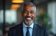 © Viktor - Smiling Black man in suit, mature businessman, pro, executive, wears blue shirt and tie. Confident leader with salt pepper beard in office setting, works for success.