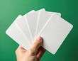 © Maryna - Hand holds stack of blank white cards against green backdrop. Empty cards ready for custom design, info or branding. Perfect for business or creative mockups.