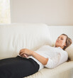 © wavebreak3 - Female reclining on pale sofa at home, wearing white blouse and black skirt, head on cushion