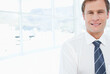 © wavebreak3 - Mid-adult man standing in office by glass windows wearing white shirt navy-blue tie, copy space